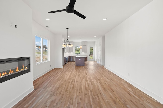 unfurnished living room featuring ceiling fan with notable chandelier and light wood-type flooring