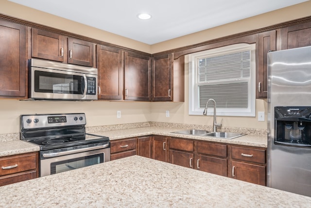 kitchen featuring dark brown cabinetry, sink, stainless steel appliances, and light stone counters