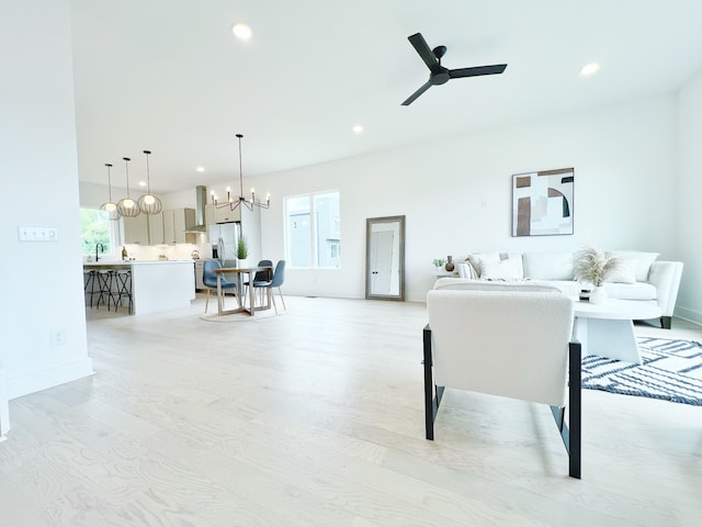 living room featuring ceiling fan with notable chandelier, sink, and light wood-type flooring