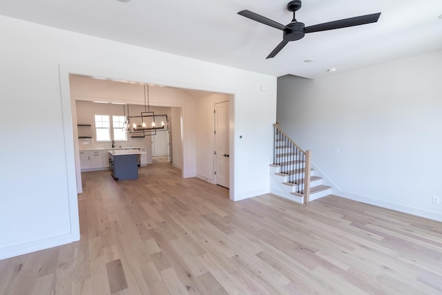 unfurnished living room featuring ceiling fan with notable chandelier and light wood-type flooring