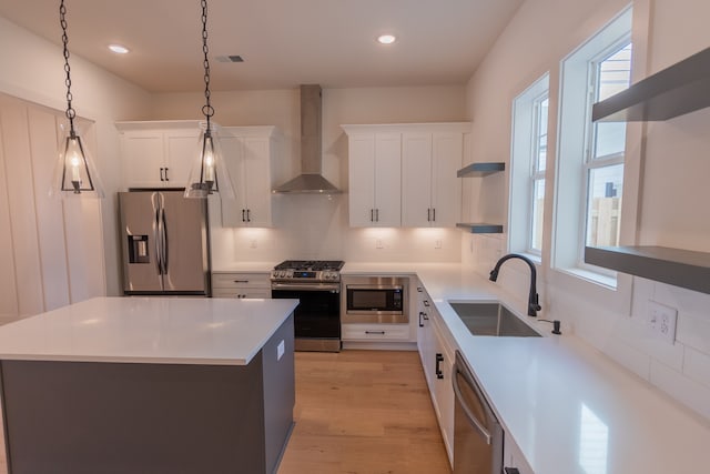 kitchen with sink, white cabinetry, hanging light fixtures, stainless steel appliances, and wall chimney exhaust hood