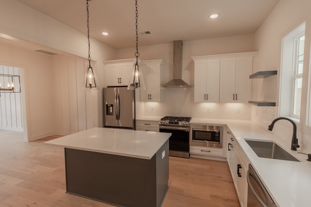 kitchen featuring a kitchen island, white cabinetry, sink, stainless steel appliances, and wall chimney range hood