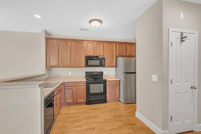 kitchen with light countertops, visible vents, light wood-style floors, a sink, and black appliances