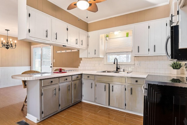 kitchen featuring sink, tile countertops, kitchen peninsula, decorative light fixtures, and white cabinets