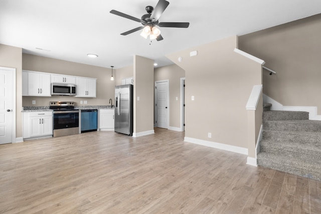 kitchen with light stone countertops, stainless steel appliances, ceiling fan, light wood-type flooring, and white cabinets