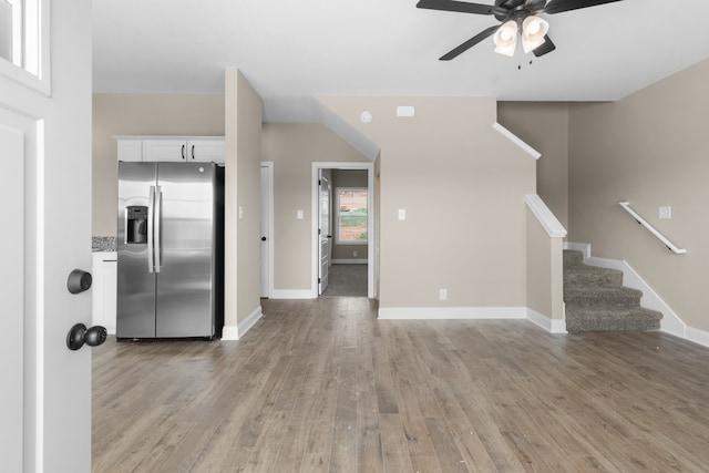 kitchen with white cabinets, light stone countertops, light hardwood / wood-style floors, stainless steel fridge, and ceiling fan