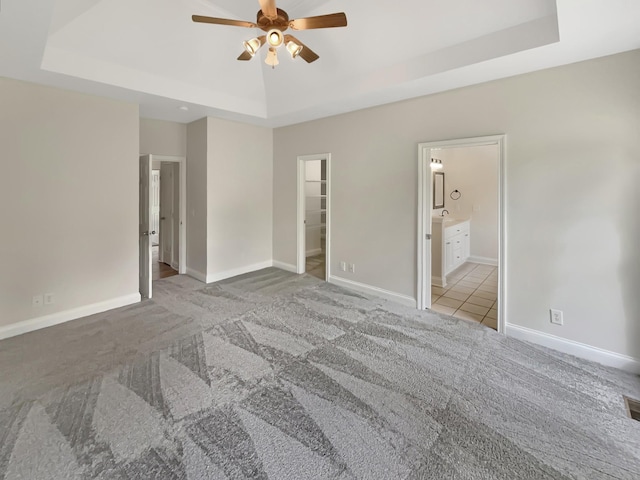 carpeted bedroom featuring ceiling fan, a tray ceiling, ensuite bath, a spacious closet, and a closet