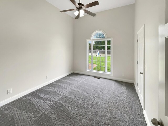 spare room featuring ceiling fan, dark carpet, and plenty of natural light