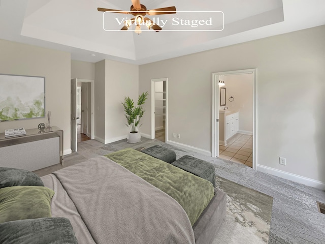 bedroom featuring a spacious closet, ensuite bath, light tile patterned floors, ceiling fan, and a tray ceiling