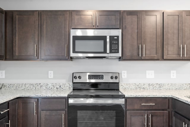 kitchen with dark brown cabinets, light stone counters, and stainless steel appliances