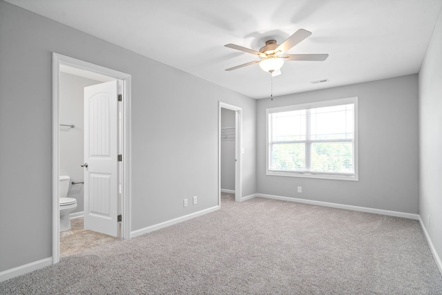 unfurnished bedroom featuring connected bathroom, a spacious closet, a closet, ceiling fan, and light colored carpet