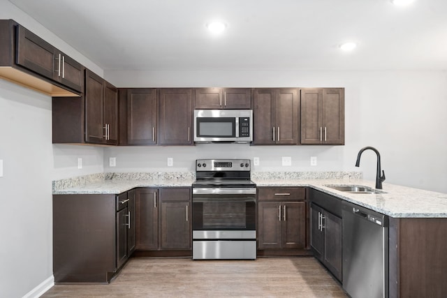 kitchen with dark brown cabinets, light wood-type flooring, a peninsula, stainless steel appliances, and a sink