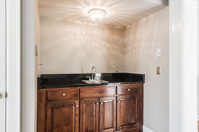 bar featuring dark brown cabinets, sink, and dark stone counters