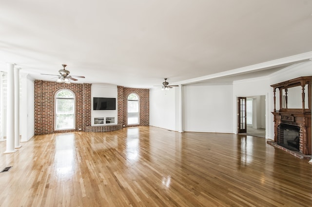 unfurnished living room with hardwood / wood-style flooring, ceiling fan, decorative columns, brick wall, and a brick fireplace