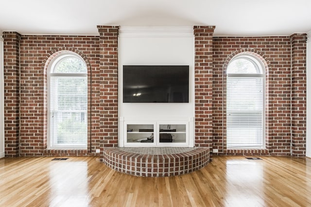 unfurnished living room with a wealth of natural light, wood-type flooring, and brick wall