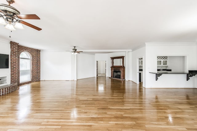 unfurnished living room with ceiling fan, crown molding, a fireplace, and light hardwood / wood-style flooring