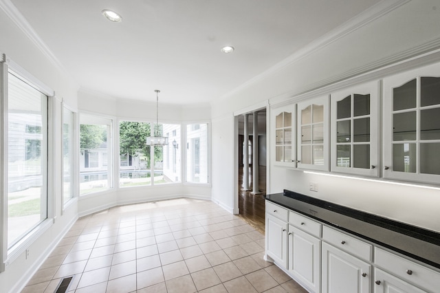 interior space with white cabinetry, hanging light fixtures, ornamental molding, light tile patterned floors, and an inviting chandelier