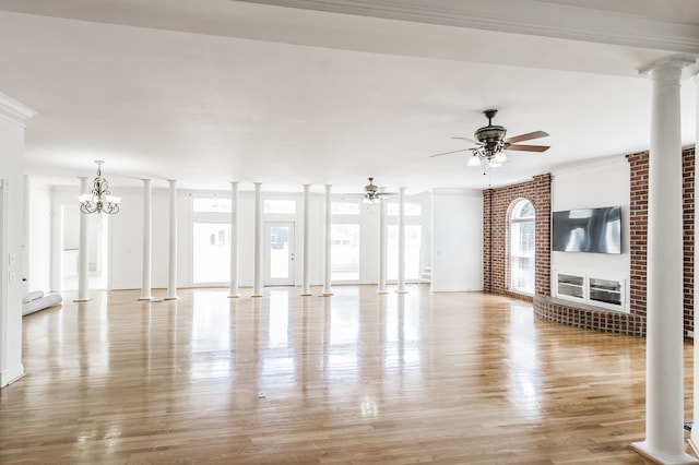 unfurnished living room featuring ceiling fan with notable chandelier, decorative columns, light hardwood / wood-style floors, and brick wall