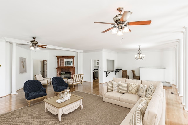 living room with ornamental molding, ceiling fan with notable chandelier, a fireplace, and light hardwood / wood-style flooring