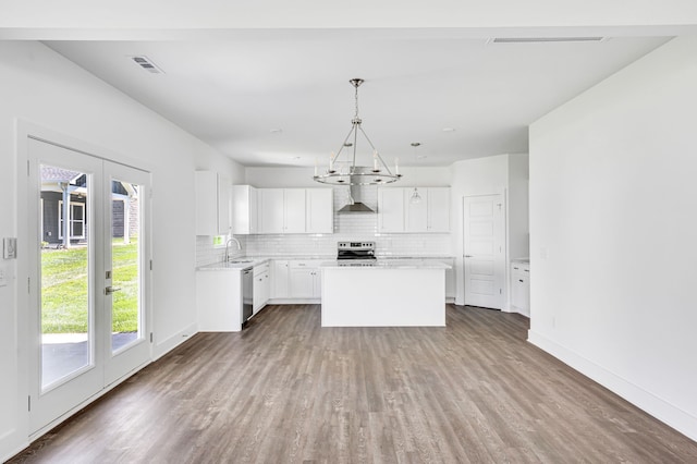 kitchen with white cabinets, dark wood-type flooring, wall chimney range hood, stainless steel appliances, and a kitchen island