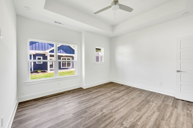 empty room with wood-type flooring, a raised ceiling, and ceiling fan