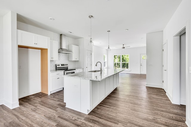 kitchen with stainless steel range with electric stovetop, wall chimney range hood, dark wood-type flooring, and an island with sink