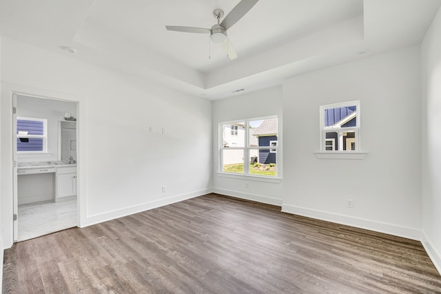 empty room with wood-type flooring, ceiling fan, and a raised ceiling