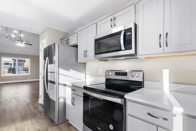 kitchen with light wood-type flooring, ceiling fan, light stone countertops, pendant lighting, and appliances with stainless steel finishes