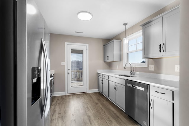 kitchen featuring stainless steel appliances, gray cabinetry, sink, and hanging light fixtures