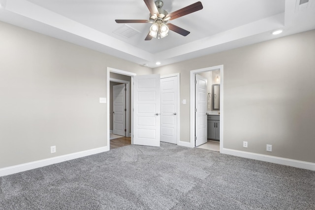 unfurnished bedroom with ceiling fan, light colored carpet, connected bathroom, and a raised ceiling