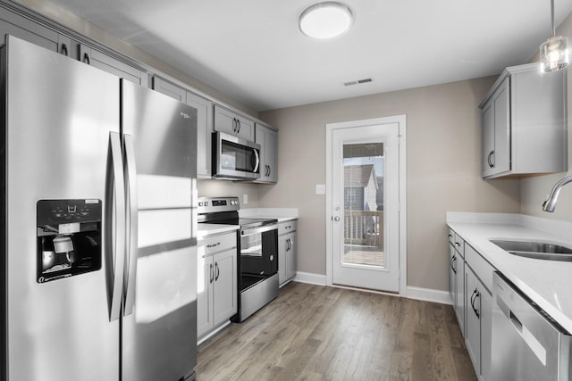 kitchen featuring light hardwood / wood-style flooring, decorative light fixtures, gray cabinets, appliances with stainless steel finishes, and sink