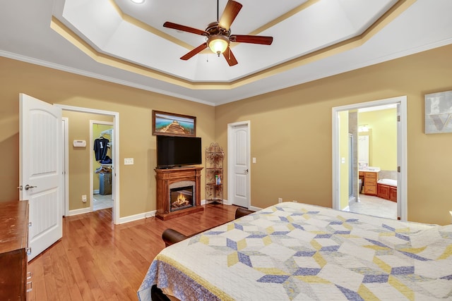 bedroom featuring wood-type flooring, connected bathroom, a tray ceiling, ornamental molding, and ceiling fan