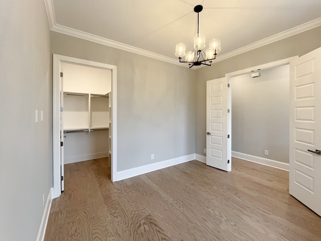 unfurnished bedroom featuring a closet, a spacious closet, ornamental molding, a chandelier, and hardwood / wood-style flooring