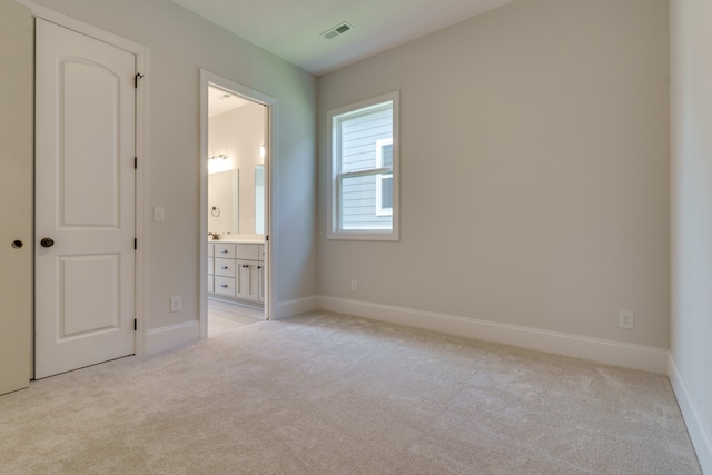 unfurnished bedroom featuring light colored carpet and connected bathroom