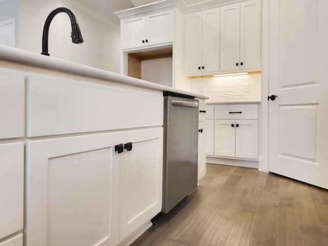 kitchen with light hardwood / wood-style flooring, crown molding, tasteful backsplash, white cabinetry, and stainless steel dishwasher