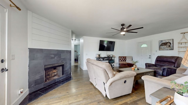 living room with a tiled fireplace, dark hardwood / wood-style floors, and ceiling fan