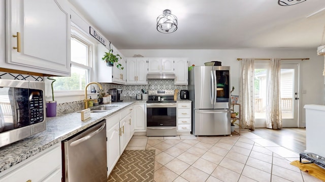 kitchen with light tile patterned floors, white cabinets, ventilation hood, stainless steel appliances, and sink