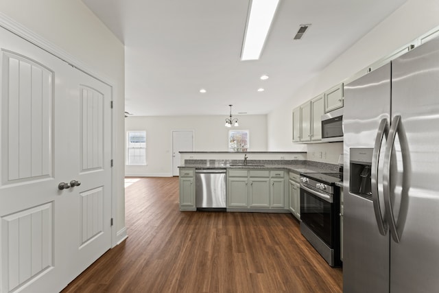 kitchen with dark hardwood / wood-style floors, hanging light fixtures, stainless steel appliances, sink, and a notable chandelier