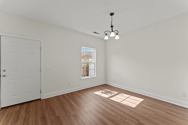 empty room with wood-type flooring and an inviting chandelier