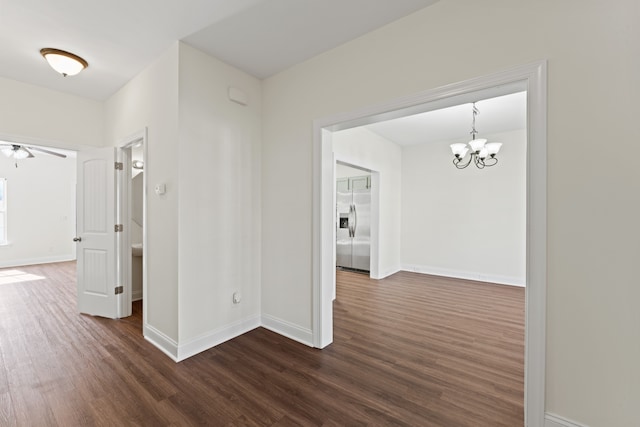 corridor with dark wood-type flooring and an inviting chandelier