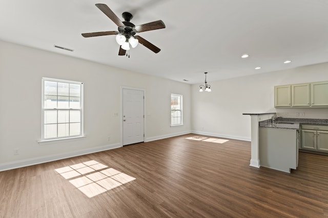 unfurnished living room featuring a wealth of natural light, ceiling fan with notable chandelier, and dark hardwood / wood-style flooring