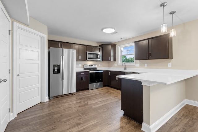 kitchen with dark brown cabinetry, kitchen peninsula, stainless steel appliances, and hanging light fixtures