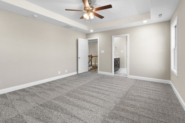 unfurnished bedroom with ceiling fan, light carpet, a tray ceiling, and ensuite bath