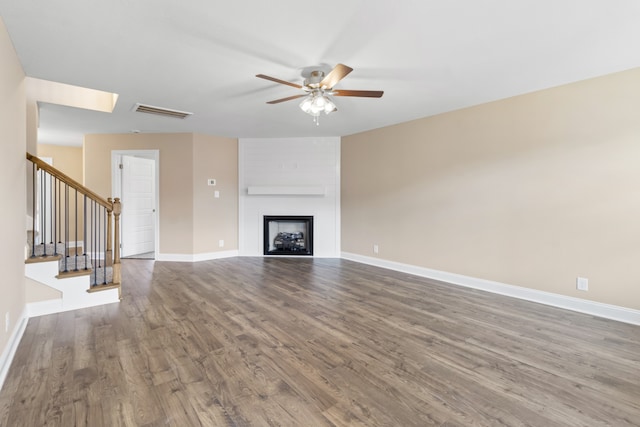 unfurnished living room with ceiling fan, a large fireplace, and wood-type flooring