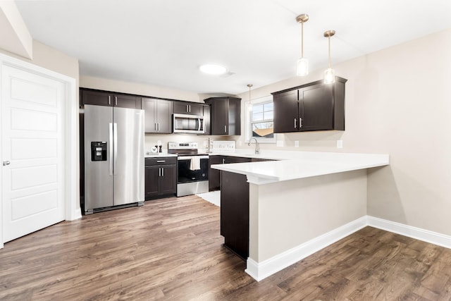 kitchen featuring pendant lighting, wood-type flooring, sink, kitchen peninsula, and stainless steel appliances