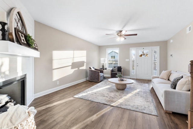 living room with a large fireplace, ceiling fan, and dark wood-type flooring