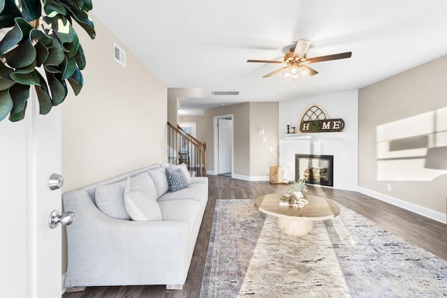 living room featuring a large fireplace, ceiling fan, and dark wood-type flooring