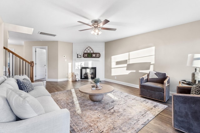 living room with ceiling fan, a fireplace, and dark wood-type flooring