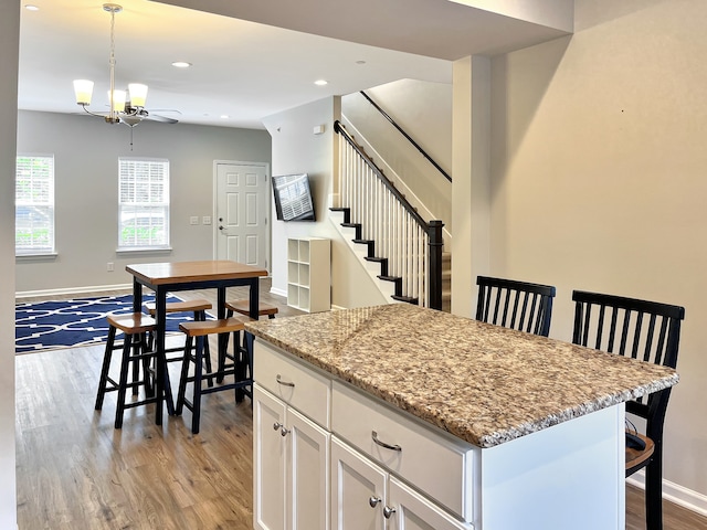 kitchen featuring light hardwood / wood-style floors, hanging light fixtures, white cabinetry, a center island, and light stone countertops