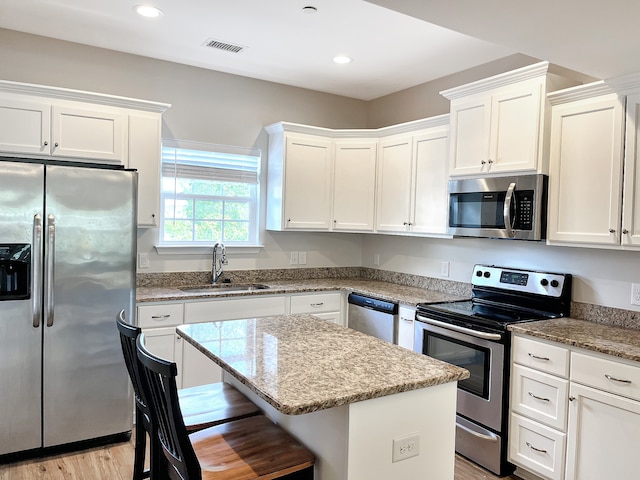 kitchen featuring light hardwood / wood-style floors, stainless steel appliances, a center island, sink, and white cabinetry